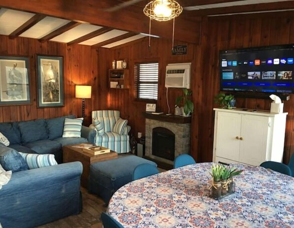 A cozy living room with a sofa, armchair, and ottoman, a fireplace, and a television mounted on the wall. - Riverfront ready for Summer Fun (Moss Point)