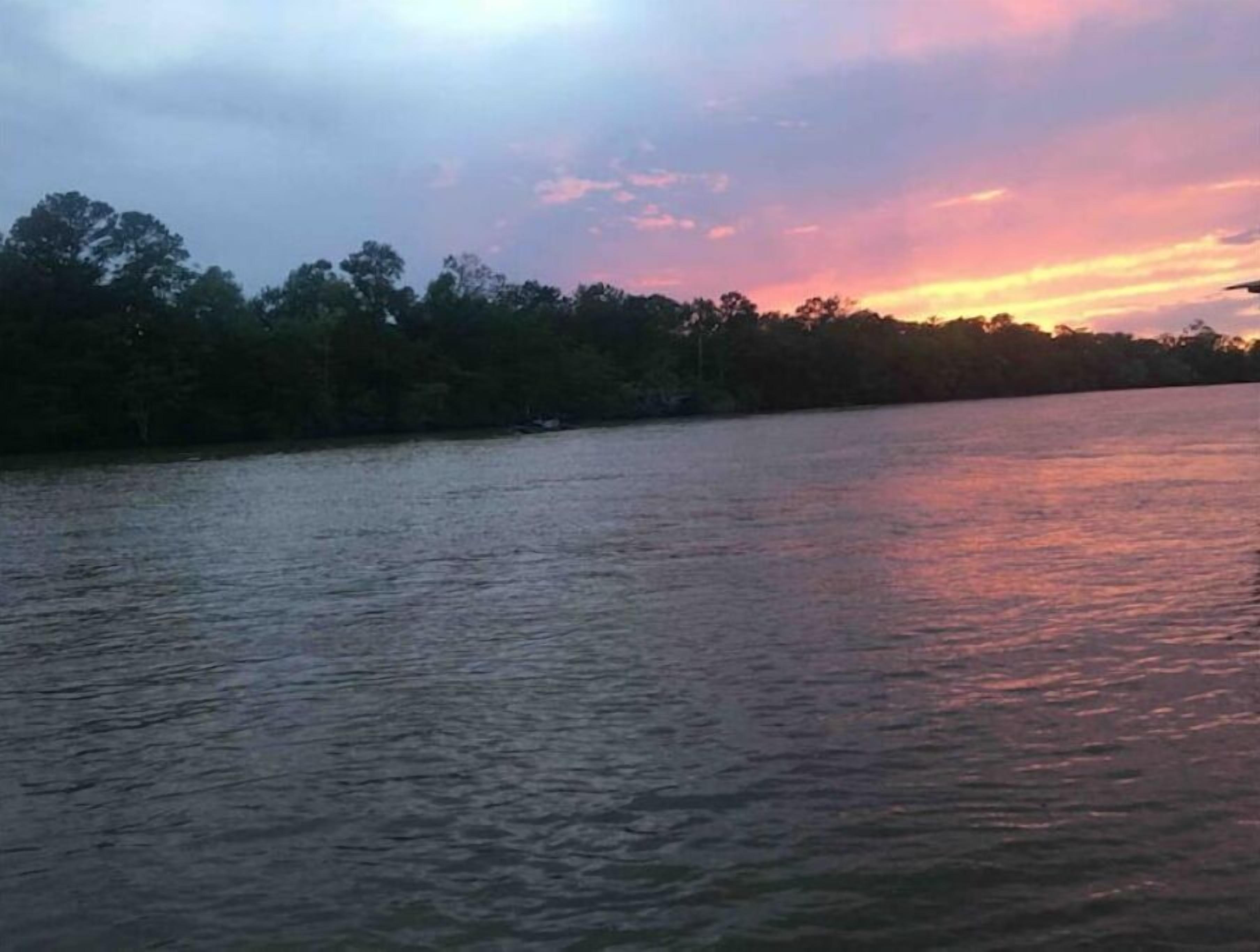 Une rivière paisible, bordée d’arbres, et un ciel au coucher du soleil.