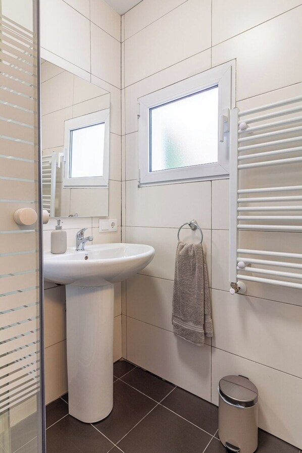 A modern bathroom with a pedestal sink, a mirror, a towel rack, and a window. - El Rincón de Cañadío · Charming Apartment in the Heart of Santander (Santander)