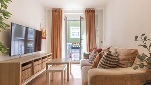 A living room with a flat-screen TV, a wooden TV stand, a beige sofa with multiple cushions, and a small white table. - El Rincón de Cañadío · Charming Apartment in the Heart of Santander (Santander)