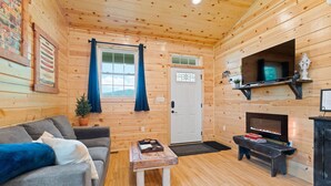 L’intérieur d’un chalet accueillant, avec un revêtement mural en bois, un canapé, une petite table, une cheminée et une porte dotée d’une fenêtre.