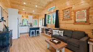 Un intérieur de chalet chaleureux, avec un revêtement en bois, un coin cuisine, un salon doté d’un canapé et un espace repas.