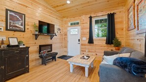 Un intérieur de chalet chaleureux avec des murs en bois, une cheminée, un canapé, une table basse et un téléviseur.