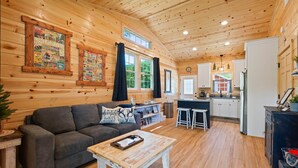 L’intérieur chaleureux d’un chalet, avec un revêtement mural en bois, un canapé, une table basse, un coin cuisine et une table à manger.