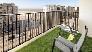 Een balkon met uitzicht op een strand en stadsbeeld, met een gazon en een stoel.