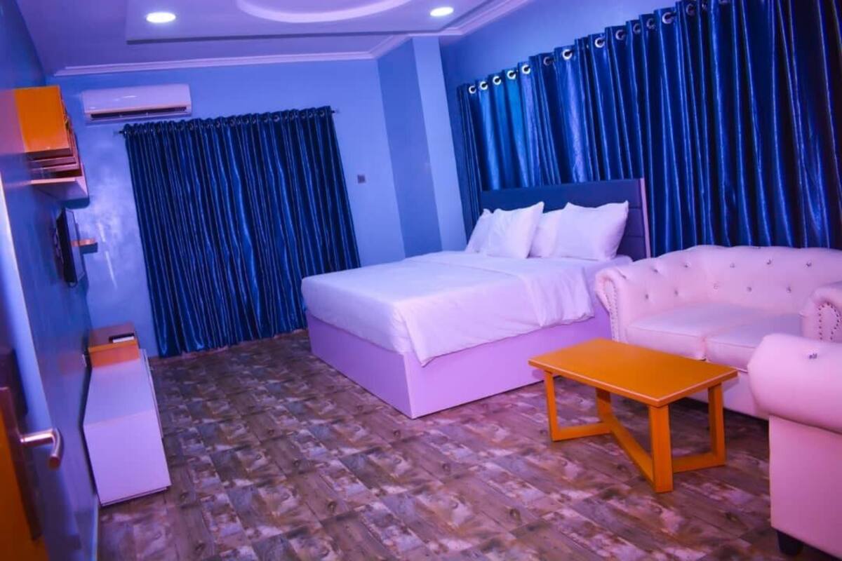 A bedroom with a bed, a sofa, a small table, and an air conditioning unit.