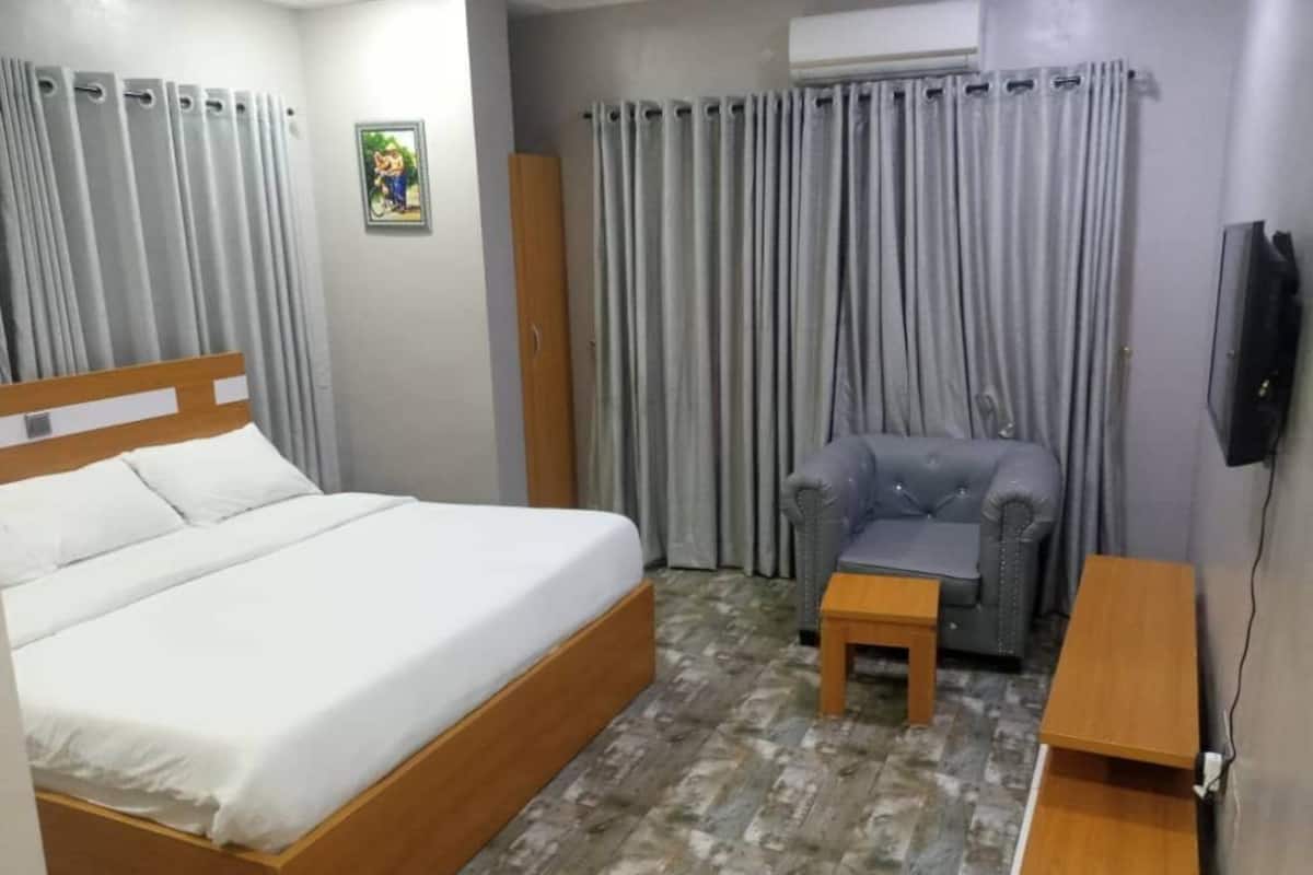 A hotel room with a bed, a small table, a chair, a TV, and curtains.