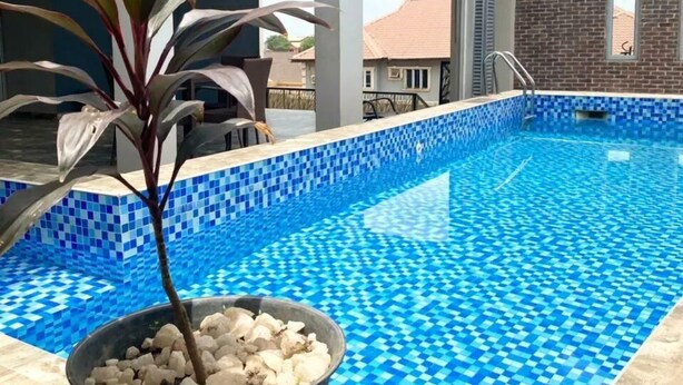 A swimming pool with blue mosaic tiles, surrounded by a covered area with pillars and a potted plant. - Camas Hotel & Suite Asero Abeokuta (Abeokuta)