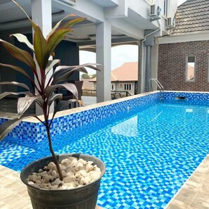 A swimming pool with blue mosaic tiles, surrounded by a covered area with pillars and a potted plant. - Camas Hotel & Suite Asero Abeokuta (Abeokuta)