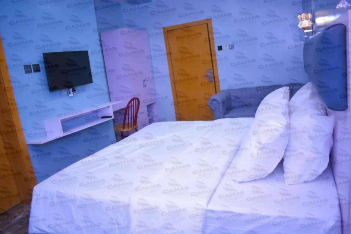 A hotel room with a bed, a TV mounted on the wall, a wardrobe, and a door.