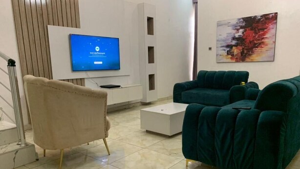 Una sala moderna con un sillón color beige, un sofá verde azulado, un televisor de pantalla plana y una mesa de centro.