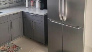 A kitchen with white cabinets, a stainless steel refrigerator, a tiled backsplash, and a patterned rug. - Le-Rendezvous A Charming 2 Bedroom 2 Bath home (Lucea)
