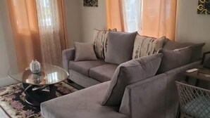 A living room with a grey sofa, a glass coffee table, and a patterned rug. - Le-Rendezvous A Charming 2 Bedroom 2 Bath home (Lucea)