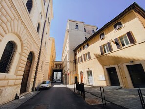 Rua estreita ladeada por edifícios históricos com portas em arco e um carro estacionado na lateral.