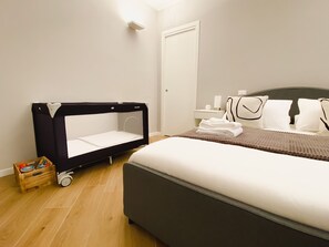 Quarto de hotel com uma cama, um berço, uma mesinha de cabeceira com abajur e uma pequena caixa de madeira.