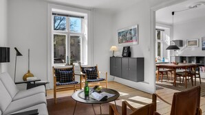 Ein modernes Wohnzimmer mit Essbereich, großen Fenstern und einer durchgehenden Tür erkennbaren Küche.
