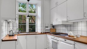 Eine moderne Küche mit weißen Schränken, einer Holz Arbeitsplatte, einem Wasserkocher, einer Spüle und einem Fenster mit Blick auf Bäume.
