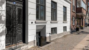 Eine Reihe weißer Gebäude mit schwarzen Türen und Fenstern, eine gepflasterte Straße und ein geparktes Auto.