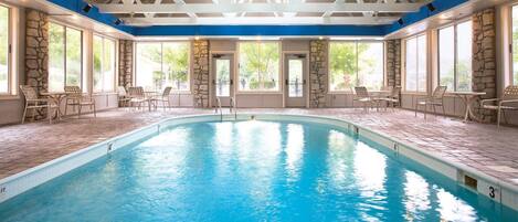 A large indoor pool with stone walls and blue ceiling beams, surrounded by outdoor seating.