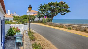 Une route côtière bordée d’un muret en pierre, avec un banc et une chaise placés sur le trottoir.