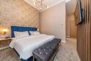 Une chambre d’hôtel moderne avec un grand lit, une table de chevet avec une lampe, un banc et un téléviseur fixé au mur.