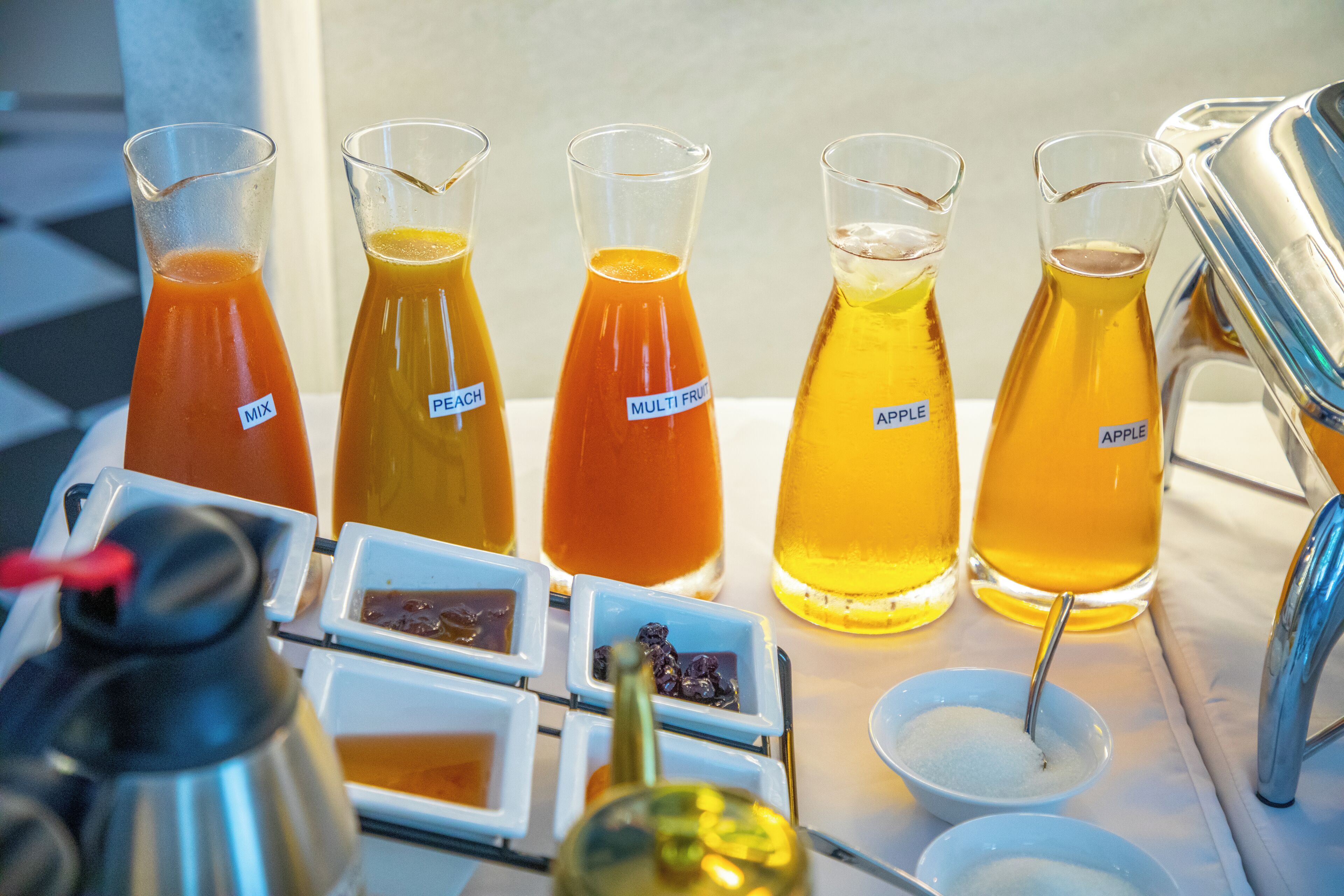 A table with various beverages and condiments, including labeled pitchers and small bowls.