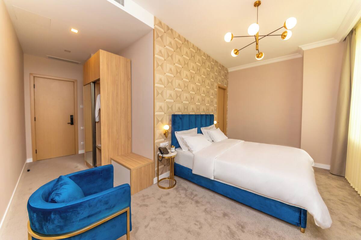 Un dormitorio moderno con una cama grande, una silla azul, un armario de madera y una pared con estampado.