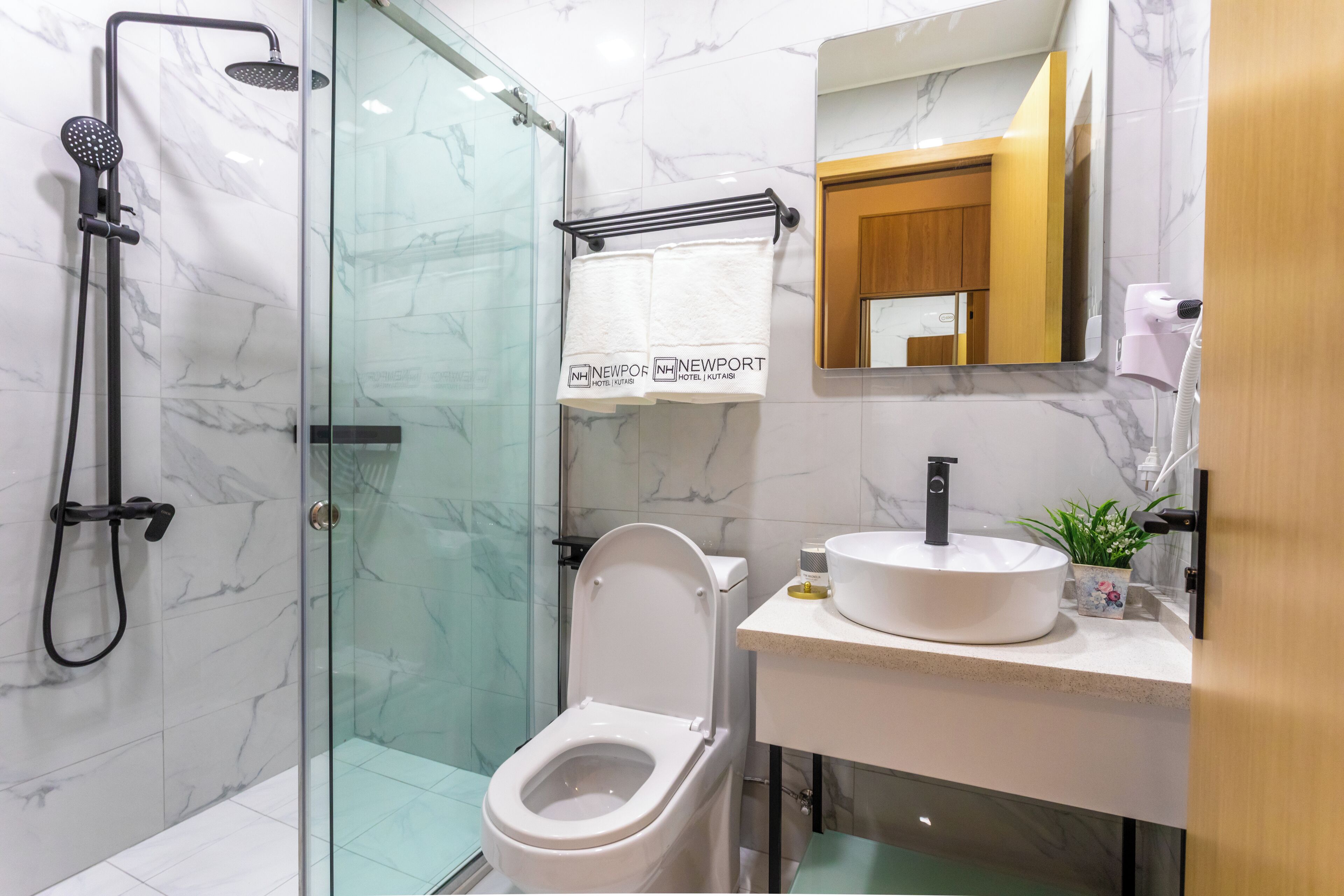A modern bathroom with a glass-enclosed shower, a toilet, a sink with a marble countertop, and a mirror above the sink.