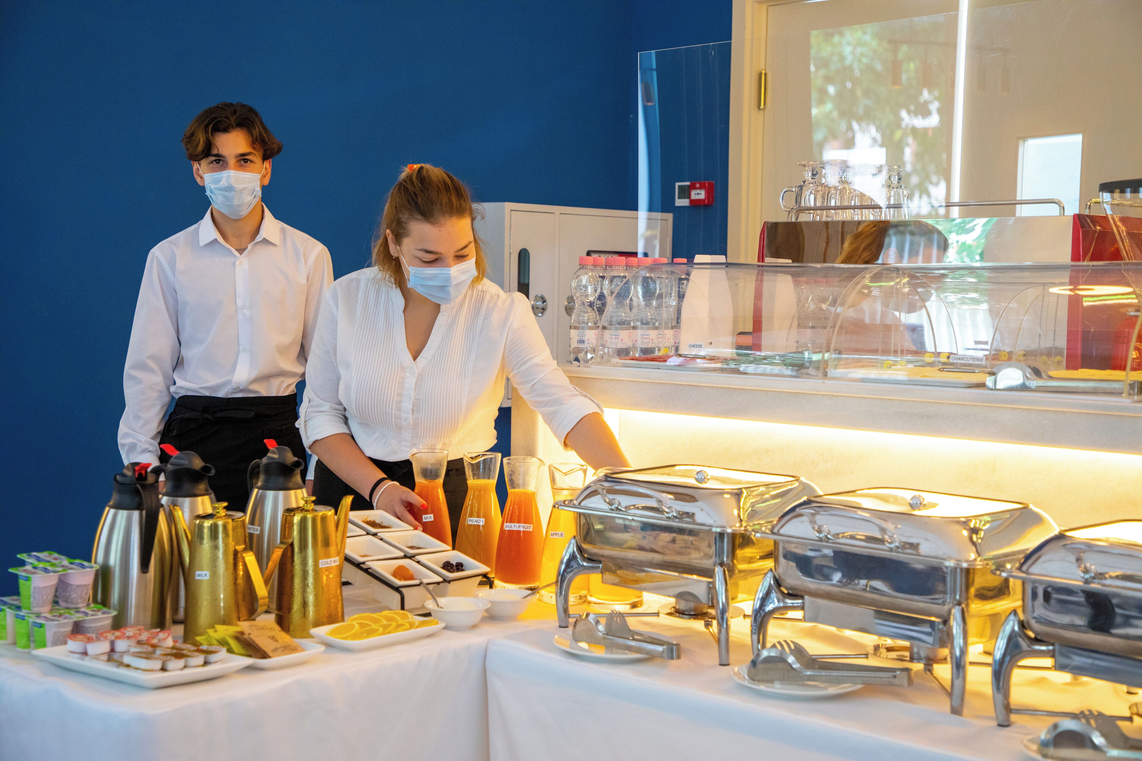 Ein Buffet mit verschiedenen Speisen und Getränken, einer Anrichte und einer blauen Wand im Hintergrund.