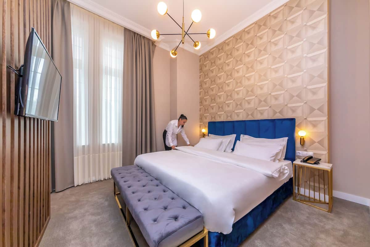 Habitación de hotel con una cama grande, un banco, un televisor montado en la pared y un papel tapiz con diseño geométrico.