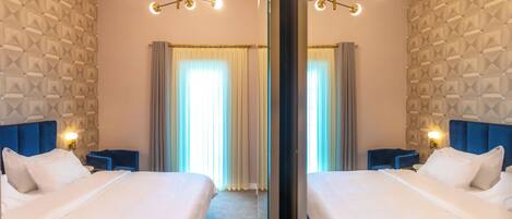A mirrored hotel room with two beds, a blue headboard, a wall with geometric pattern, and a chandelier.