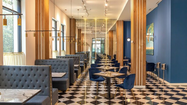 Un restaurante moderno con suelo a cuadros, asientos azules y grises, y una barra larga.