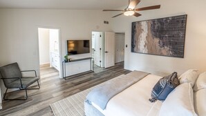 Een moderne slaapkamer met een bed, een stoel, een bureau, een televisie en een plafondventilator.