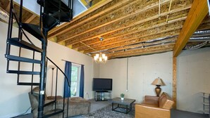 A living room with a wooden ceiling, a black spiral staircase, a flat-screen TV, a sofa, a coffee table, and a lamp. - Lake Front, Sunrise, Dock, Kayaks + Game Room (Cadiz)