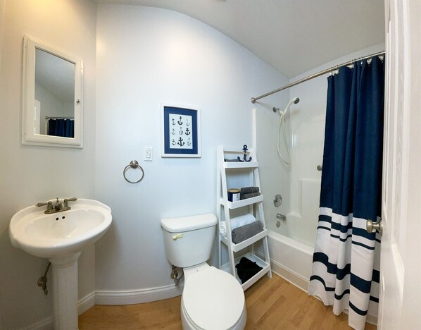 A bathroom with a sink, toilet, and shower. There is a towel rack, a framed picture on the wall, and a shower curtain.