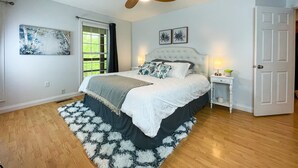 A bedroom with a bed, a ceiling fan, a window, a door, and a nightstand with a lamp. - Lake Front, Sunrise, Dock, Kayaks + Game Room (Cadiz)