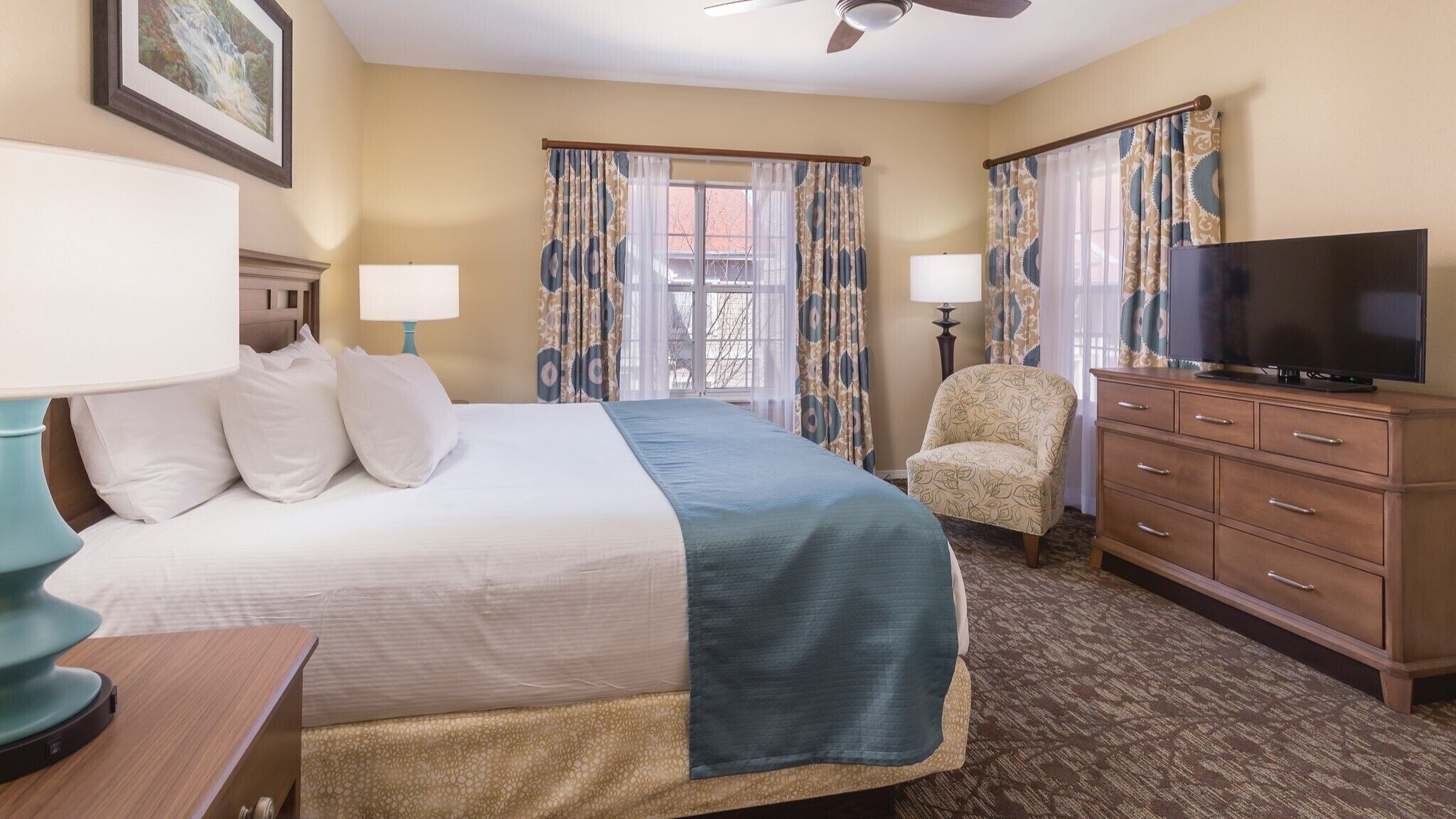 Una habitación de hotel con cama, televisión, silla, escritorio y lámpara.