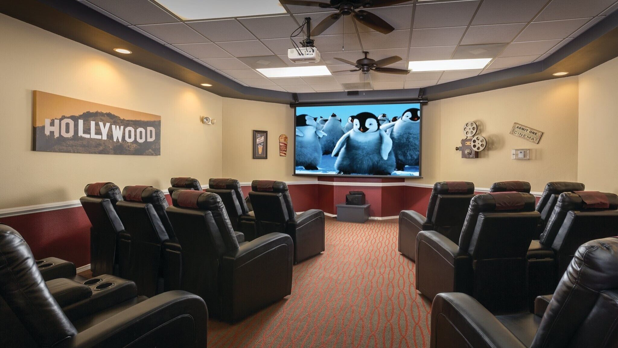 Una sala home theater con diverse poltrone reclinabili in pelle, un'ampia televisione a schermo piatto, un ventilatore a soffitto e una decorazione a tema 'Hollywood'.