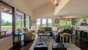 Un salon spacieux avec de grandes fenêtres, un coin salon confortable et une cuisine à l’arrière-plan.
