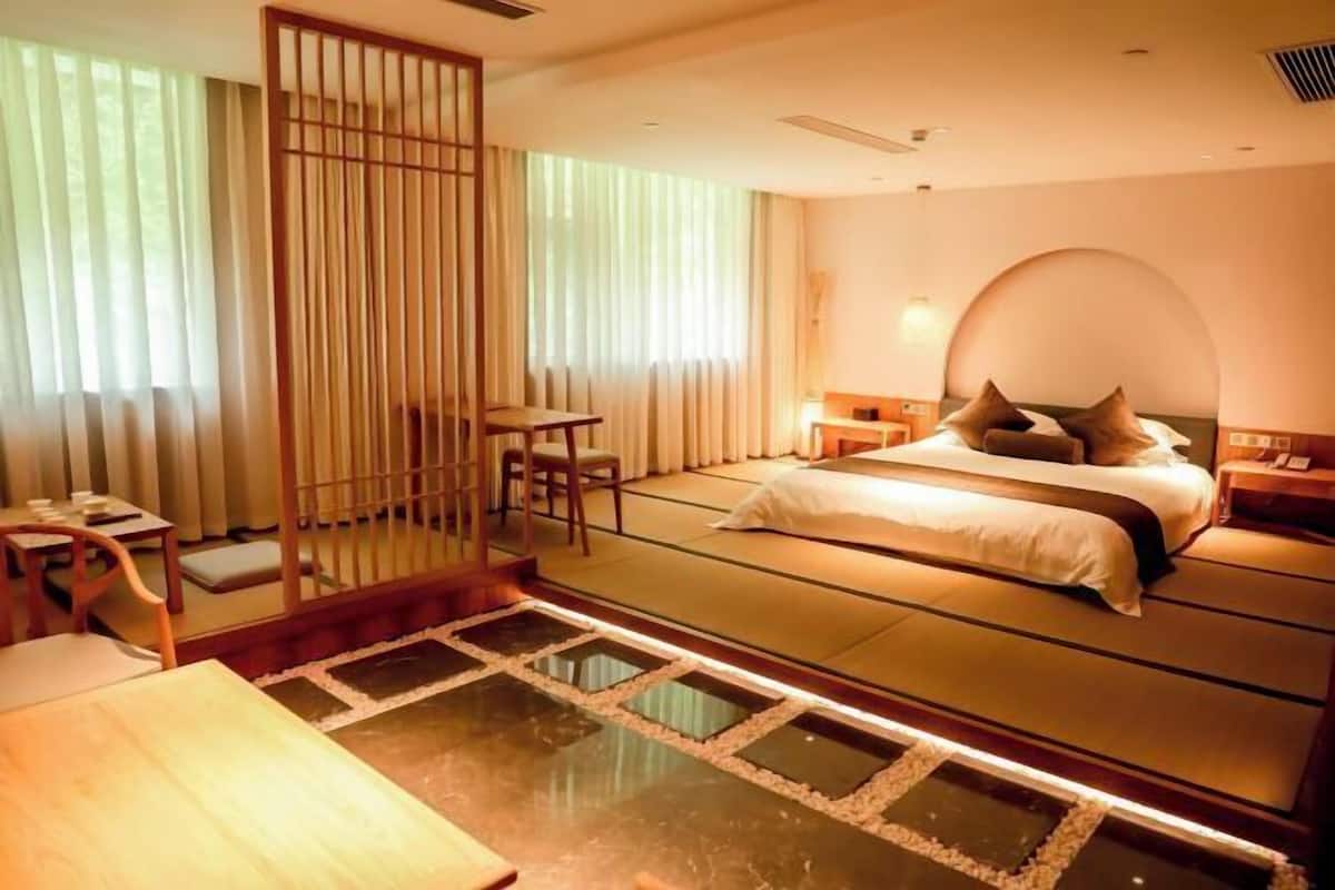 Une pièce de style japonais traditionnel, avec un sol recouvert de tatamis, un lit bas, une porte coulissante et une petite table entourée de chaises.