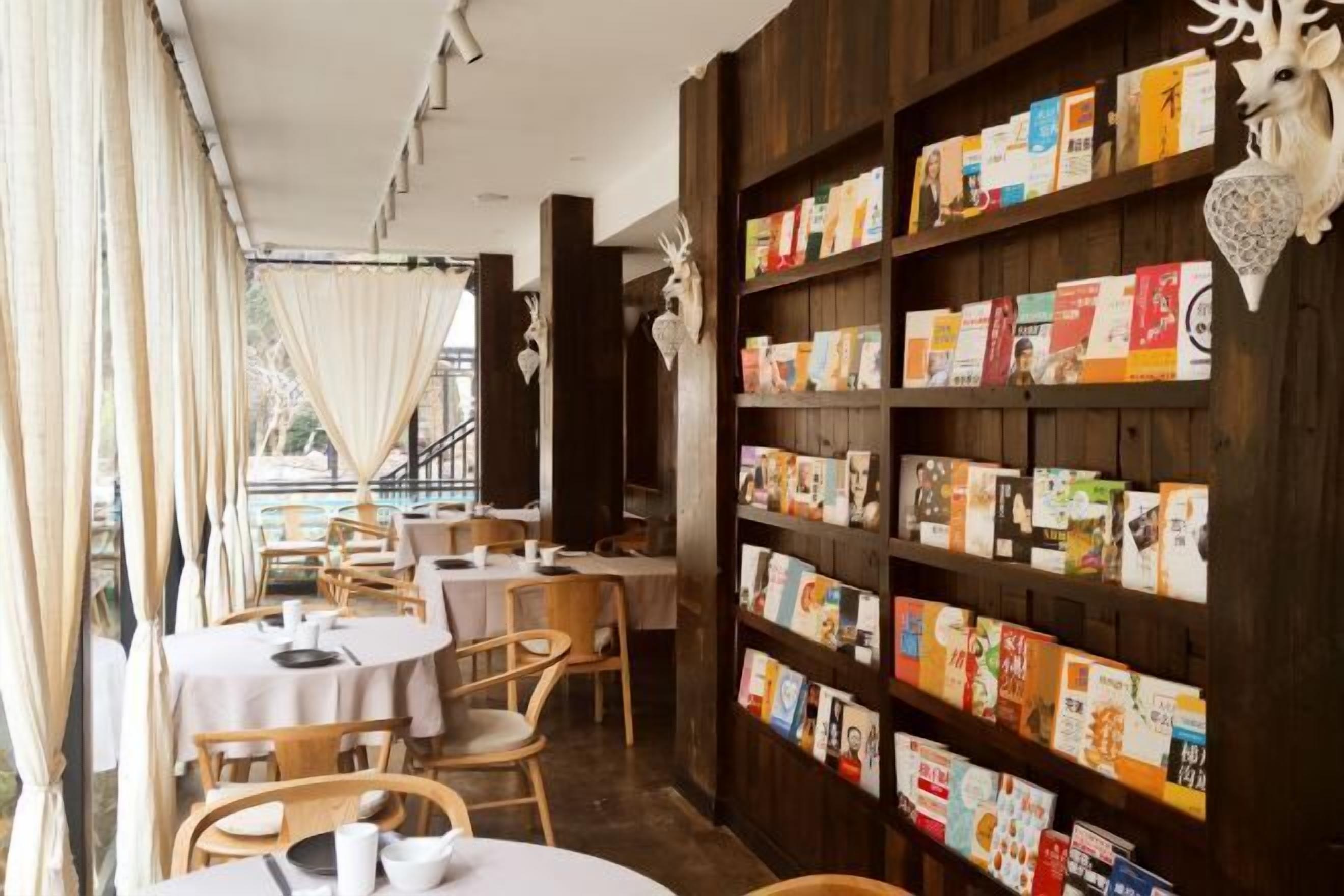 A cozy restaurant with wooden walls, a bookshelf filled with books, and tables set for dining.