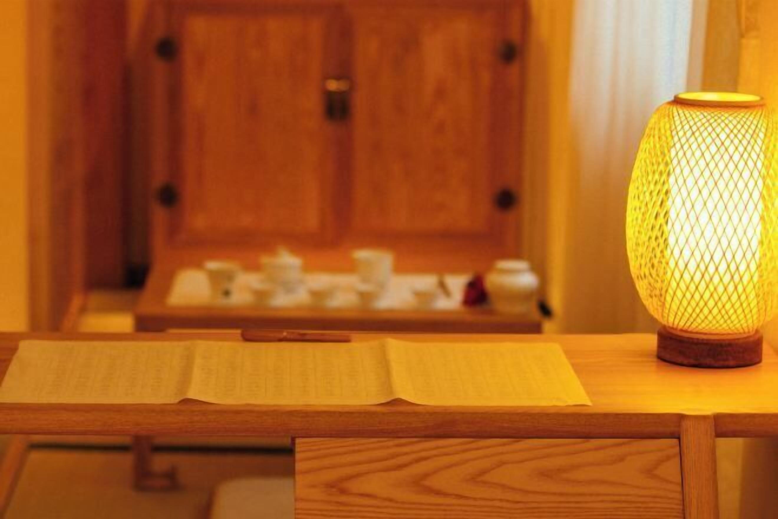 A wooden table with an open book and a lit lamp.