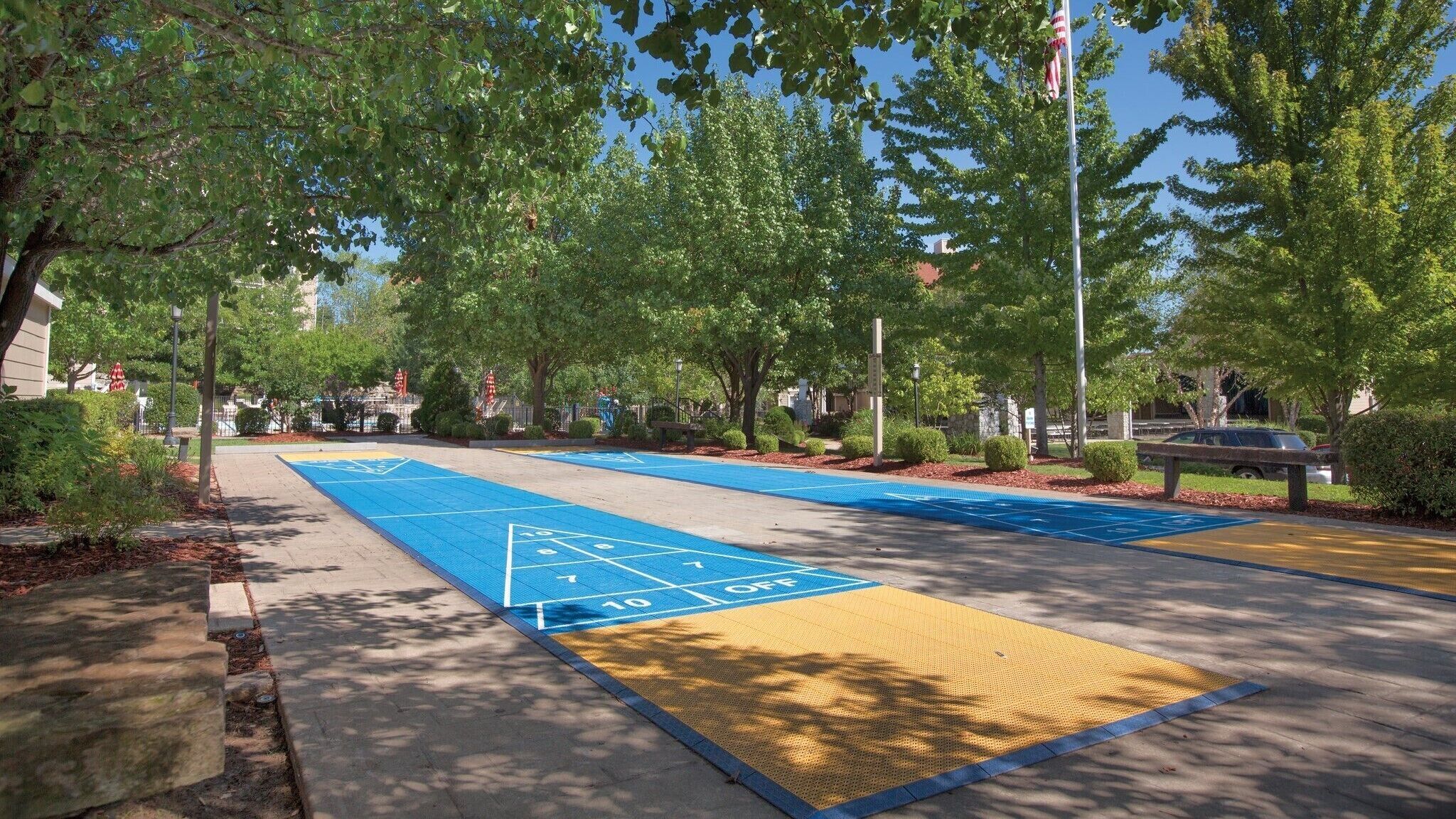 Ein Park mit einem Shuffleboardfeld, Bäumen und einem Fahnenmast.