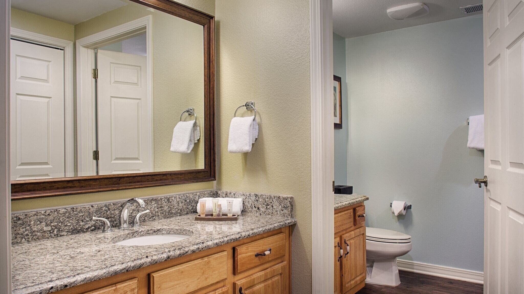 A bathroom with a granite countertop sink, wooden vanity, and a white toilet.