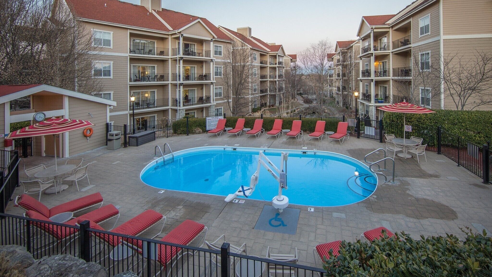 A swimming pool with lounge chairs and umbrellas, surrounded by multi-story buildings with balconies.