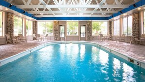 En stor indendørs swimmingpool med stenvægge og blå loftsbjælker, omgivet af udendørs siddepladser.