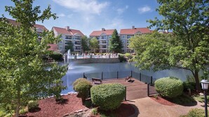 Udsigt over en sø til et resort med træterrasse, springvand og poolområde med liggestole.