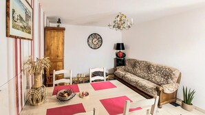 A living room with a sofa, chairs, a table with red placemats, a clock, a lamp, and a chandelier.