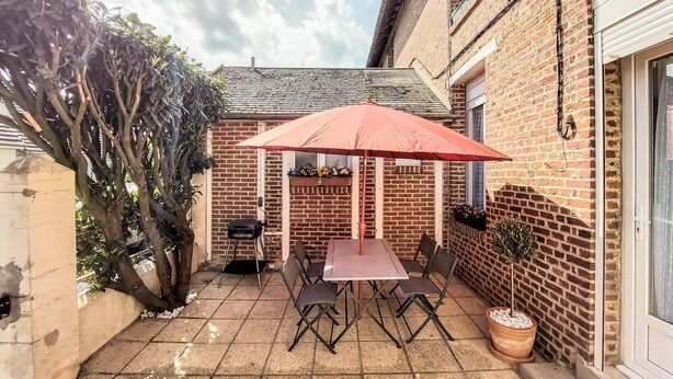 A patio with a table and chairs, a red umbrella, and a brick wall.