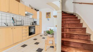 A kitchen with wooden cabinets, a stove, and a sink. There is a staircase leading to another level.